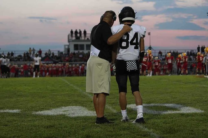 shutterstock_2029495961 football coach with arm around player number 84 on sideline