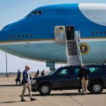 Security detail near blue and white aircraft with staircase and SUV