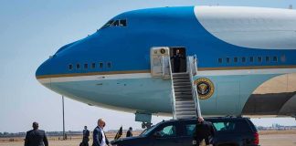 Security detail near blue and white aircraft with staircase and SUV