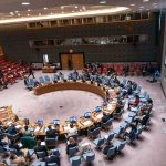 Delegates seated around a circular conference table in a large chamber