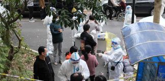 Christian Jones and others wait at an outdoor COVID-19 testing site with staff in protective suits