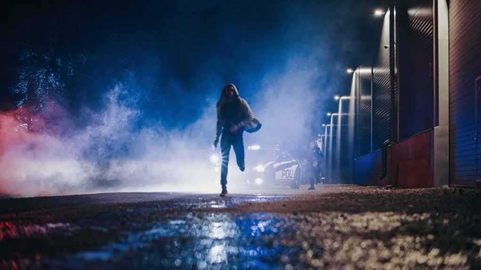shutterstock_2232055289 Person running at night near police car with flashing lights