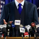 Trump’s Media Ban Sparks Constitutional Firestorm A speaker at a press conference with multiple microphones in front of them