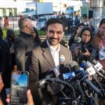 Zohran Mamdani speaks at a press conference; Julia Bacha is visible among the crowd