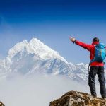 Hiker with arms raised facing snowy mountain peak