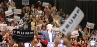 Donald Trump speaks at a rally podium as a large crowd cheers; Orel Hershiser, Ion Marin, and Billy Joe DuPree present