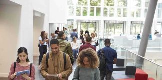 Students walking through a bright campus lobby using mobile devices