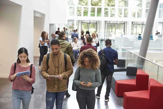 shutterstock_478513882 Students walking through a bright campus lobby using mobile devices