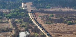 Border fence and patrol road cutting through dry landscape with sparse trees
