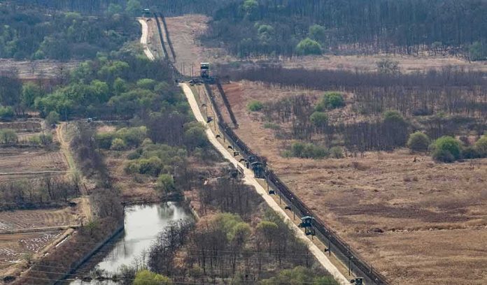 shutterstock_624870374 Border fence and patrol road cutting through dry landscape with sparse trees