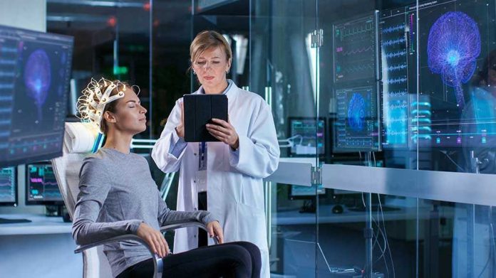 1036798276 Patient wearing EEG cap sits while clinician reviews data on tablet
