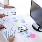Polling Errors Could Change Midterms Business hands reviewing charts with a calculator and monitor on desk