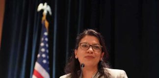 Rashida Tlaib speaking at a podium with a U.S. flag in the background