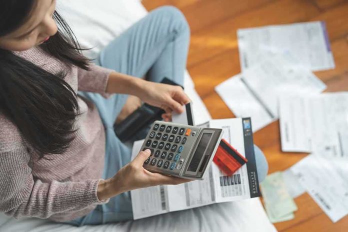 shutterstock_1511121023 Woman using a calculator while reviewing bills on the floor