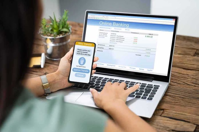 shutterstock_1542438851-1 Person using smartphone to approve bank transfer beside laptop with online banking