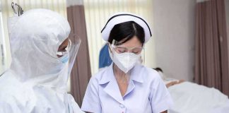 Lab Worker Dies as Plague Questions Swirl nurse in PPE writing on a clipboard with colleague