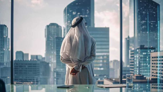 shutterstock_2113523906 Man in traditional robe looking out office window at modern skyscrapers