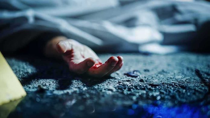 Human hand on gritty ground near a covered body