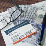 Medicare card on paperwork with cash, glasses, and a pen