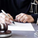 Legal Battle Sparks Controversy Judge writing at desk with gavel and Lady Justice statue