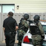 Federal Search Intensifies Probe Into Omar police officers in tactical gear beside patrol car
